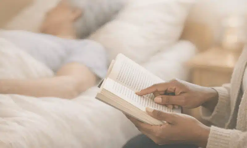 Doula de fin de vie lisant au chevet d'une personne âgée alitée – présence humaine et accompagnement palliatif dans les Yvelines