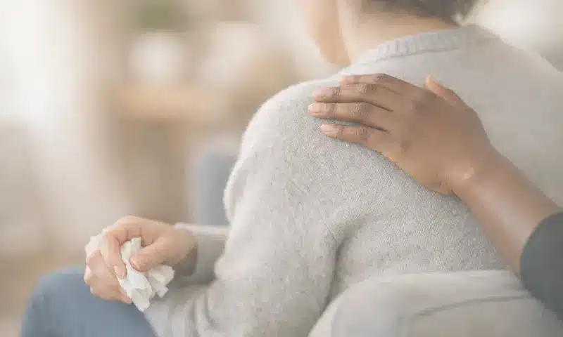 Doula posant une main réconfortante sur l'épaule d'une personne en deuil tenant un mouchoir – présence humaine et écoute non-jugeante, accompagnement du deuil dans les Yvelines (78)